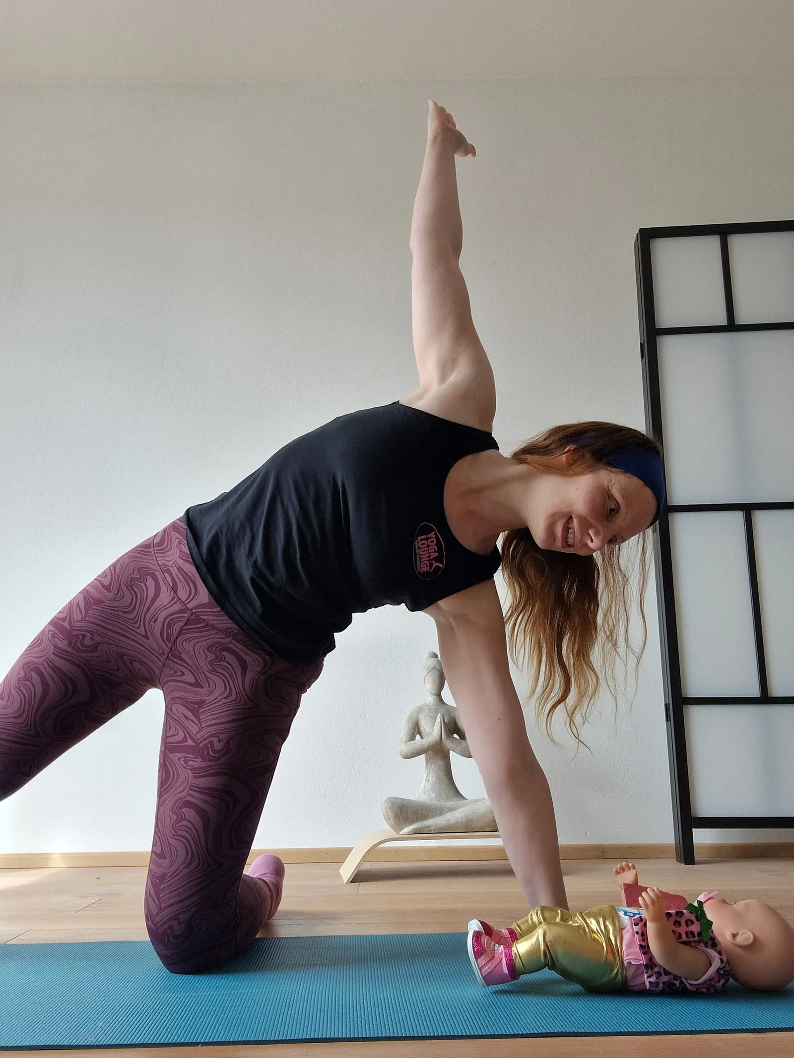 Claudia in einer Yogahaltung auf der Matte, neben ihr eine Babypuppe