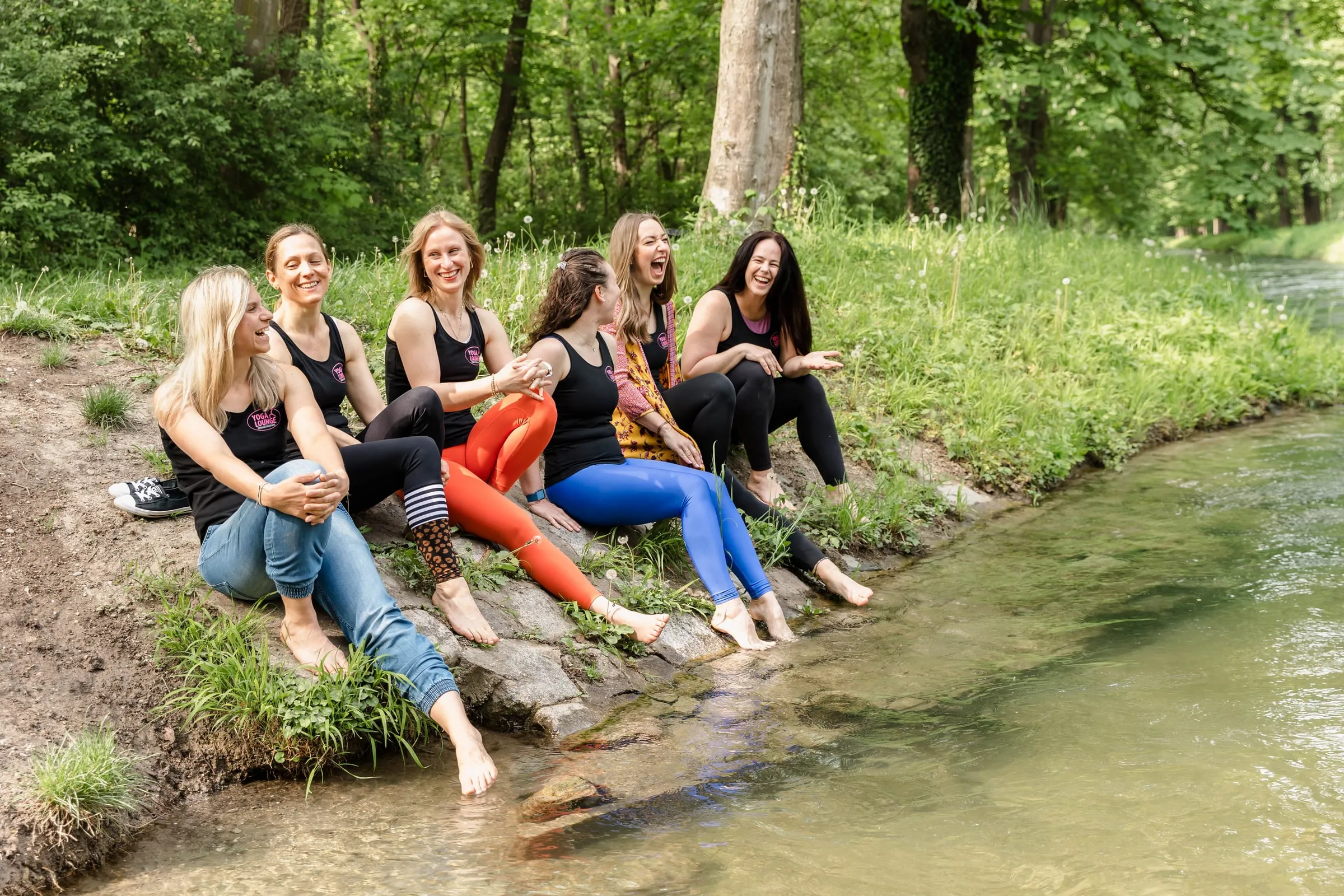 Yogalehrerinnen sitzen lachend mit den Füßen im Bach