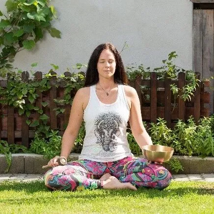 Madlen meditiert im Schneidersitz mit einer Klangschale im Garten