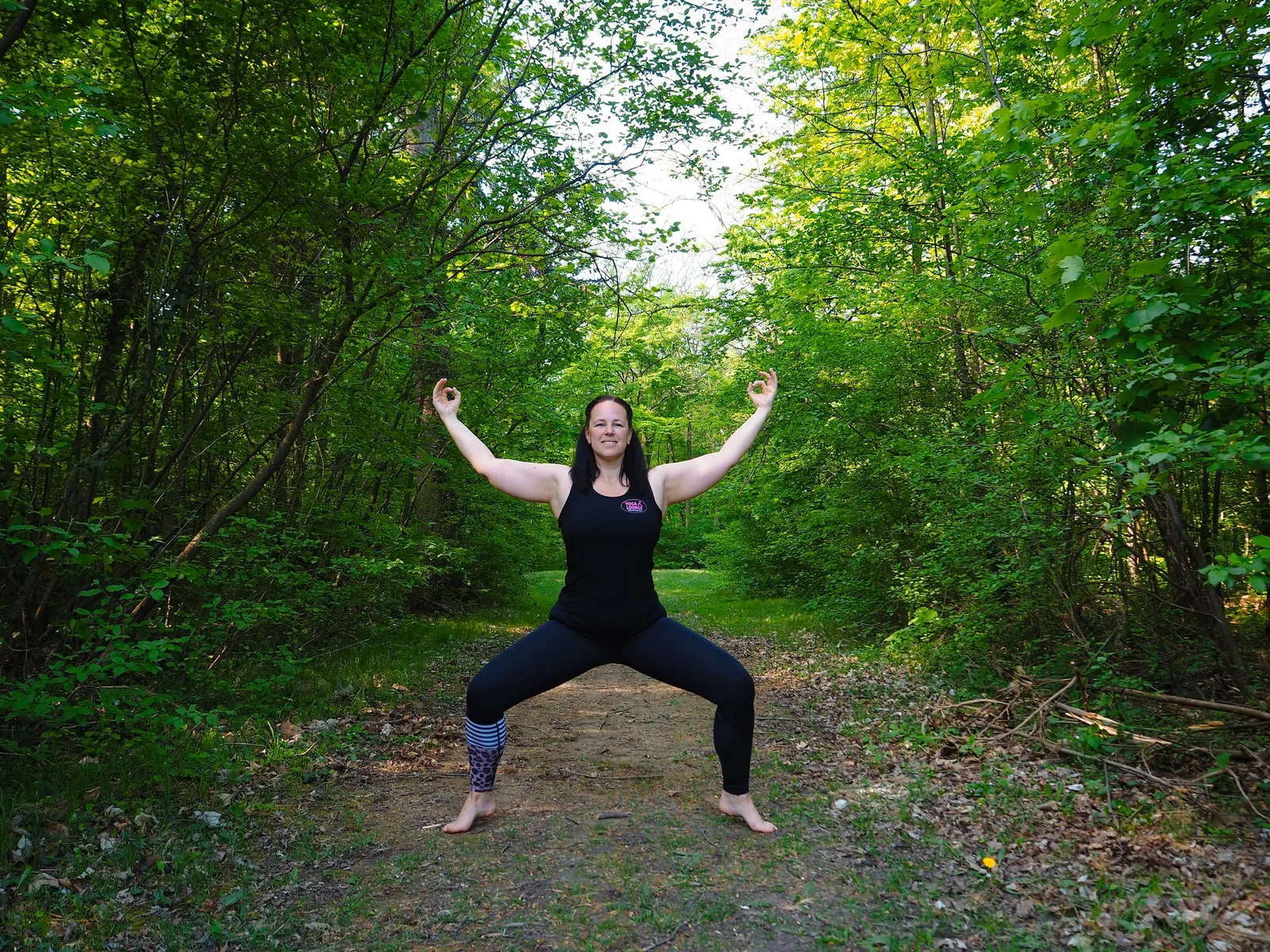 Yogalehrerin in der Göttinnen-Haltung auf einem Waldweg