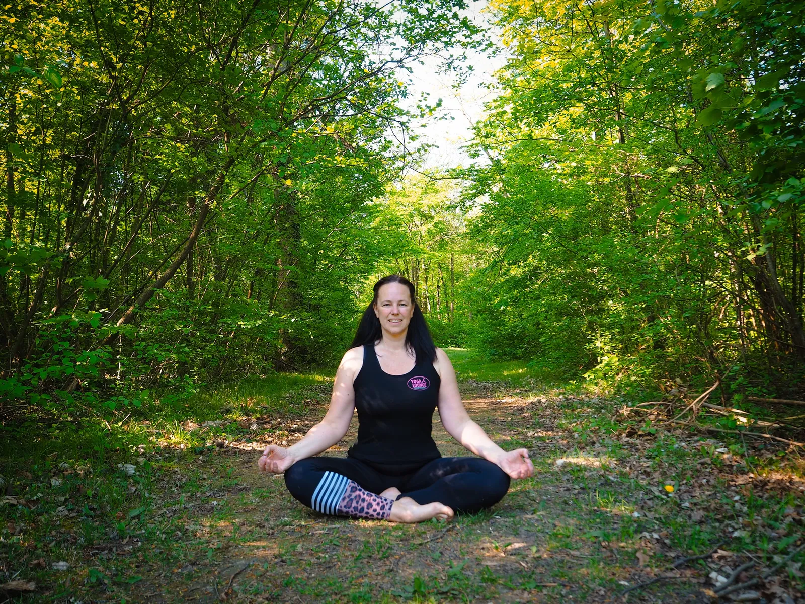 Yogalehrerin meditiert im Schneidersitz auf einem Waldweg